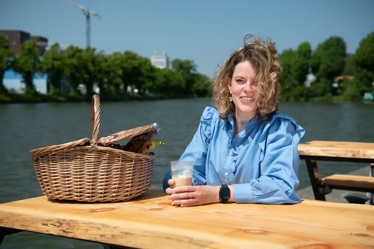 vrouw zit met picknickmand aan een tafel bij het water